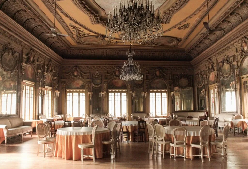 Salle de banquet historique à Turin, tables rondes nappées et lustres.