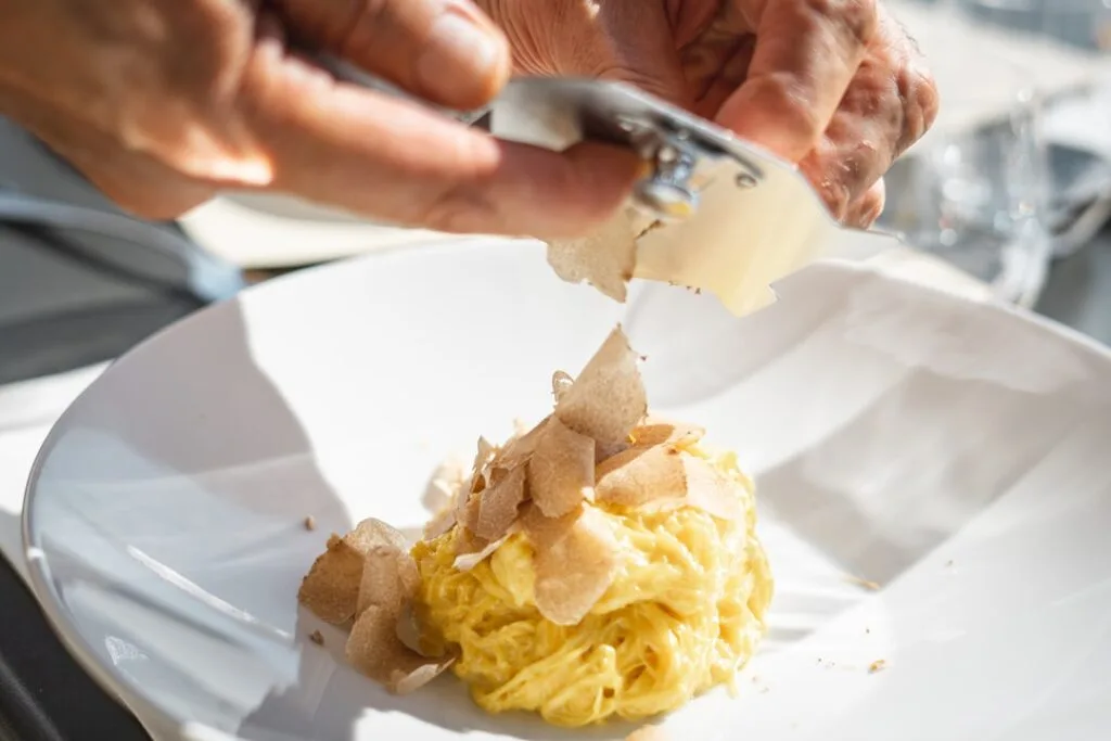 Mains d'un chef râpant des truffes sur pâtes crémeuses piémontaises