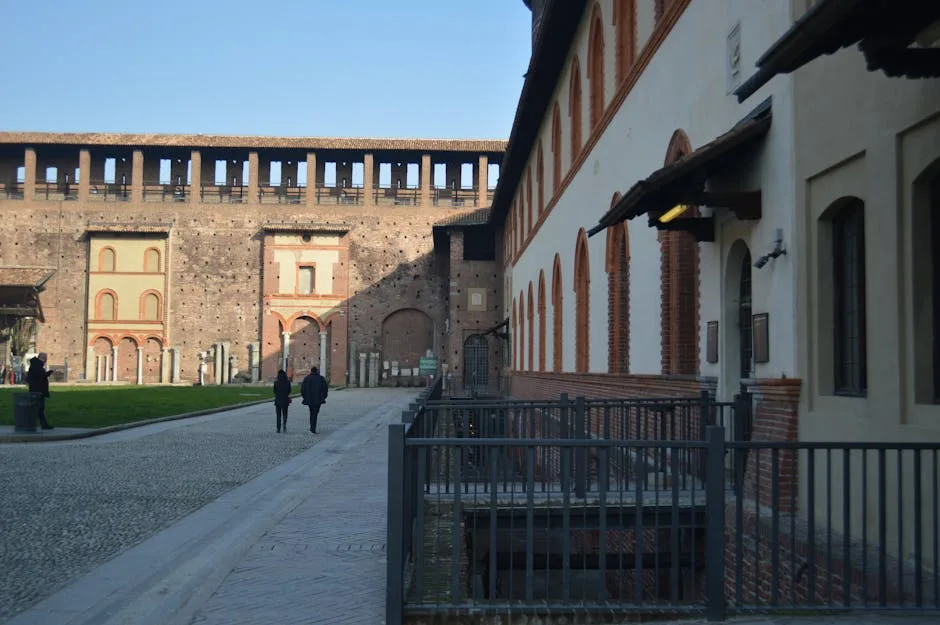 Cour pavée bordée de bâtiments en briques, deux personnes marchant