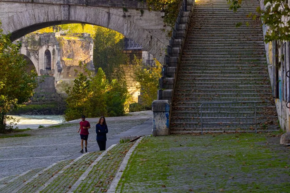 Joggeur et promeneuse sur la rive pavée du Po à Turin, sous un pont