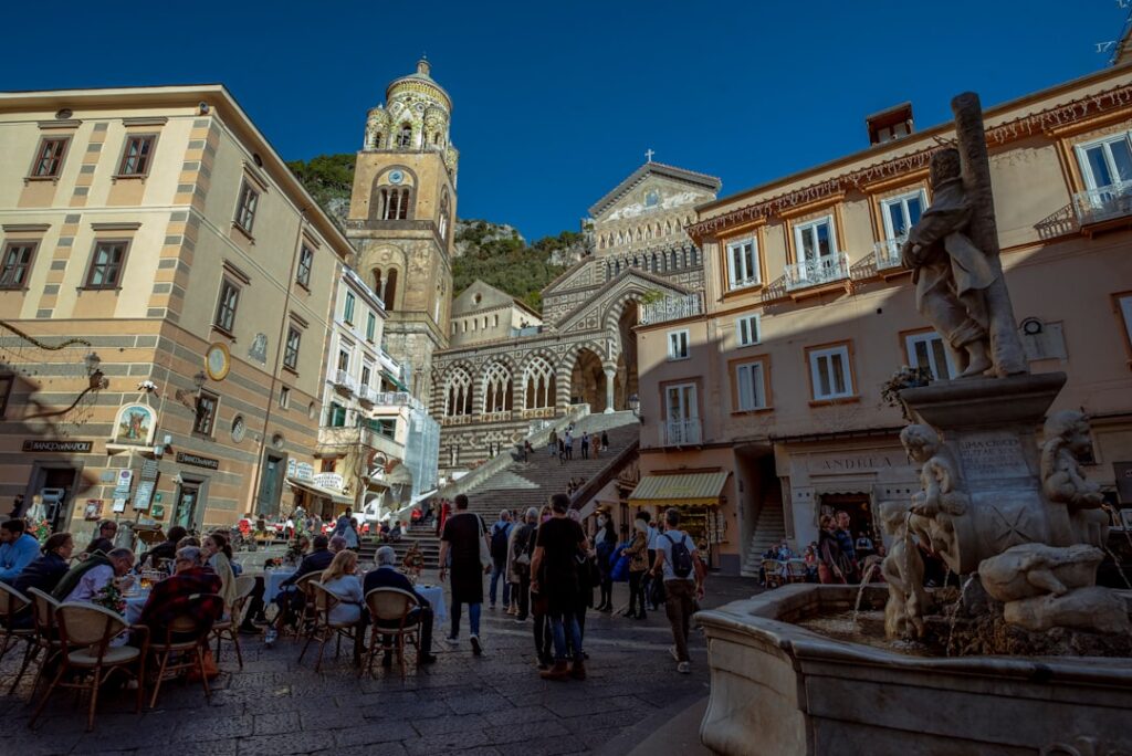 Druk plein met terrasjes en de Duomo van Amalfi aan zee