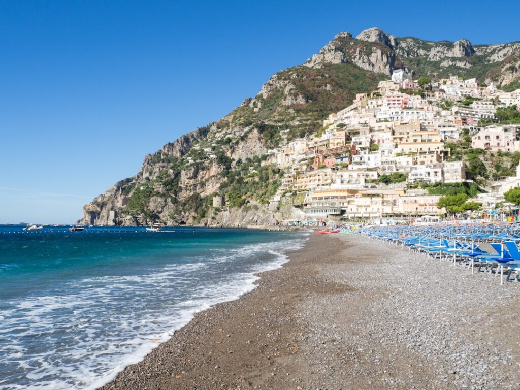 Leerer Kiesstrand mit Reihen blauer Sonnenschirme in Positano, Côte amalfitaine