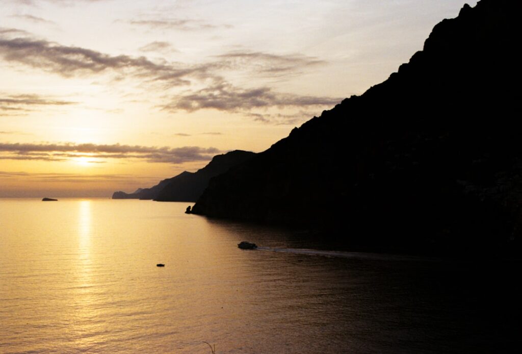 Tramonto sul mare con scogliere della Costiera Amalfitana e barca solitaria