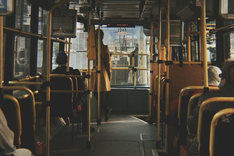 Binnenkant van een bus met zittende reizigers en gele handgrepen