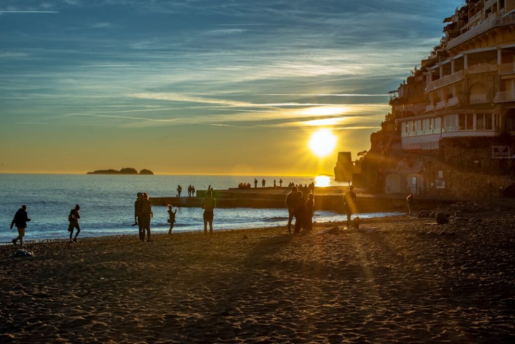 Silhouetted figures on a beach with low sun near Amalfi Coast cliffside