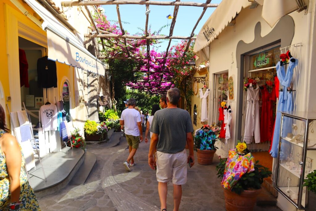 Schmale Einkaufsstraße mit Bougainvillea und Touristen in einem Küstendorf der Côte amalfitaine.