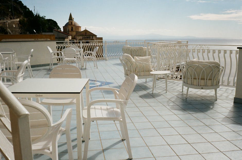 Sunlit rooftop terrace with white chairs and distant Amalfi church tower