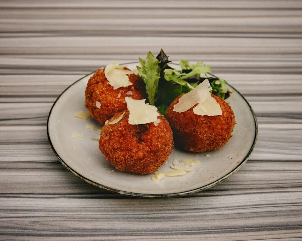Trois arancini croustillants garnis de copeaux de fromage, style Palerme