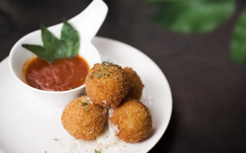 Boules d'arancini dorées servies avec coulis de tomate et basilic