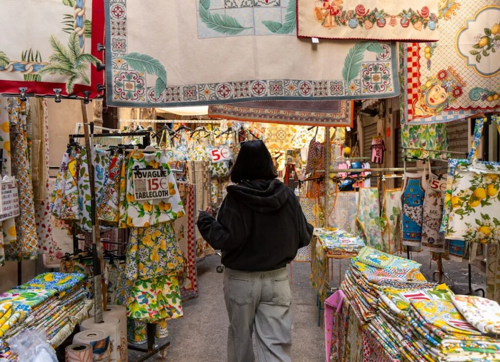 Personne de dos dans une ruelle de Palermo entourée de nappes colorées