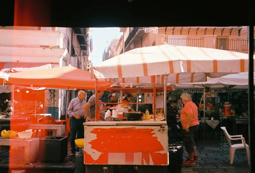 Étals de marché avec parasols orange et clients dans une rue de Palermo