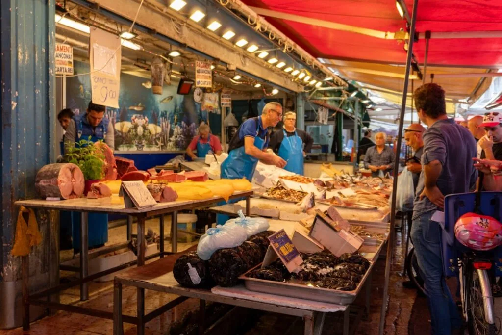 Étal de poissons animé au marché Ballarò de Palermo, vendeurs en tabliers.