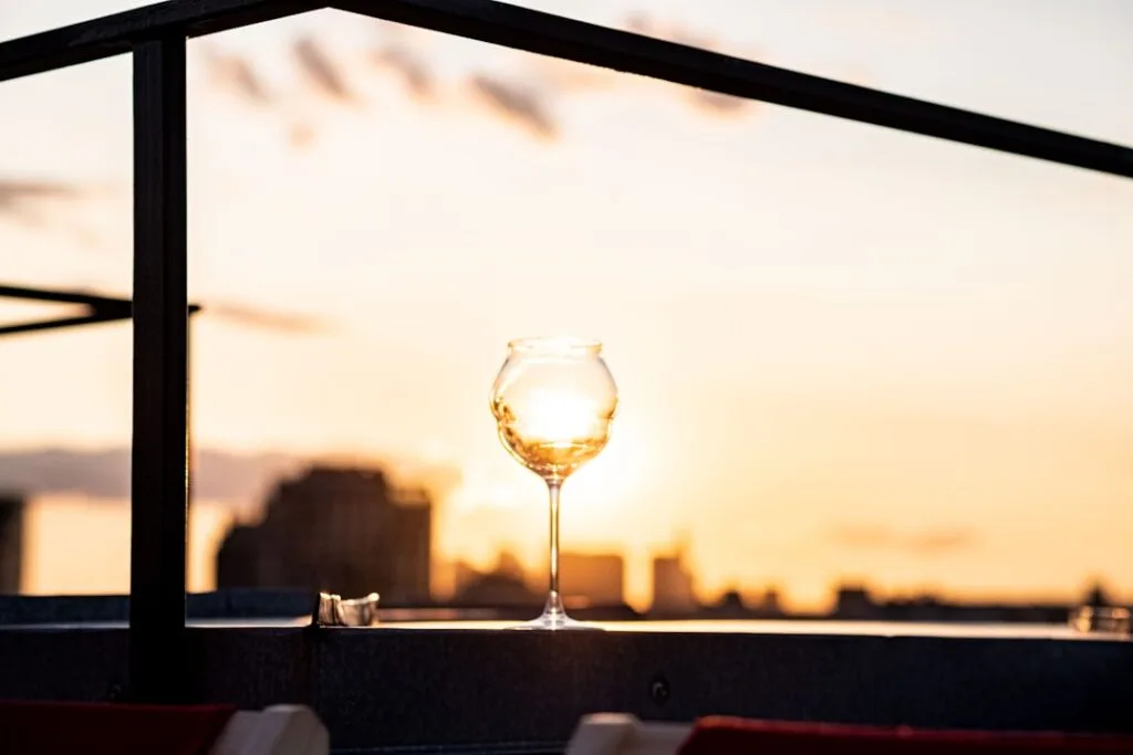 Verre posé sur la rambarde, soleil couchant reflété, vue sur Palermo