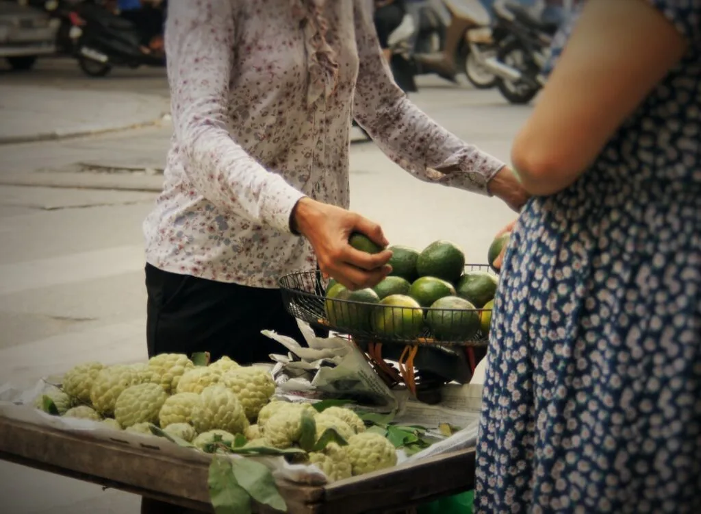 Vendeuse choisissant des avocats près d'un chariot de corossols à Palermo.