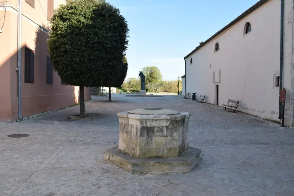 Petit puits de pierre sur une place dégagée, statue en arrière-plan à Palermo