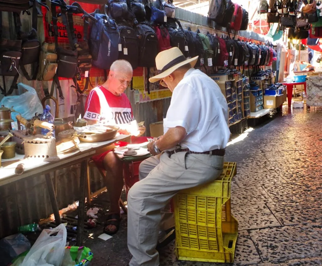 Deux hommes assis au marché de Palermo entourés d'ustensiles