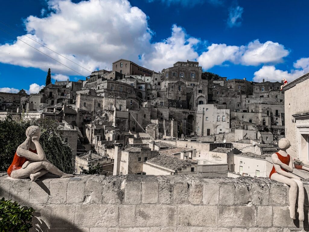 Skulpturen in roten Badeanzügen auf Mauer vor den Sassi von Matera