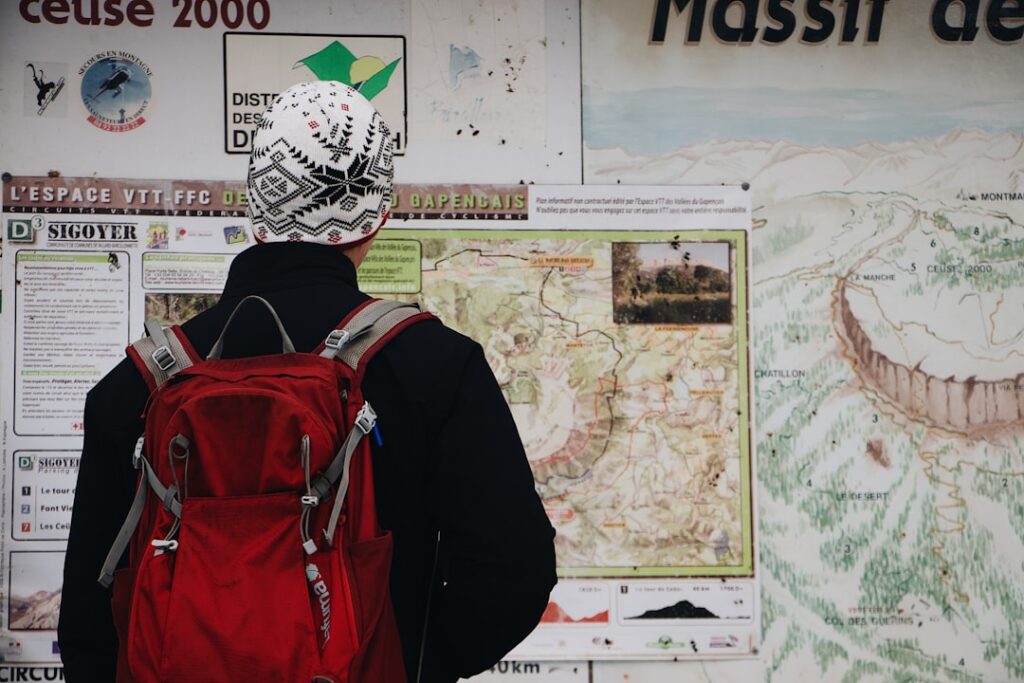 Person mit rotem Rucksack liest große Wanderkarte auf Informationstafel