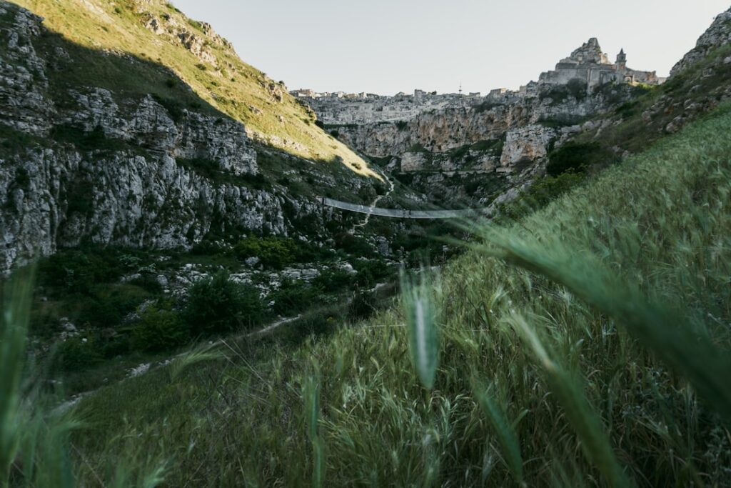 Grüne Schlucht mit Hängebrücke und Matera-Siedlung am Horizont