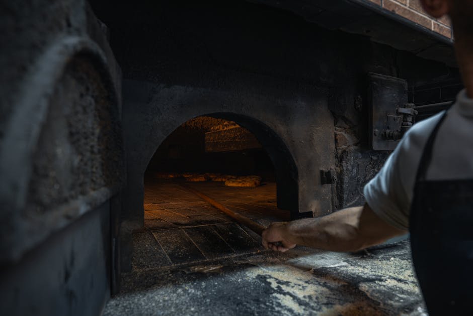 Hand eines Bäckers schiebt Brot in traditionellen Steinofen