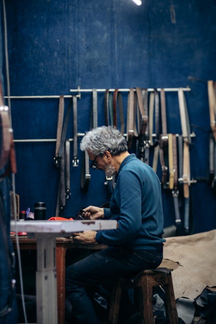Artisan crafting leather belts against a blue workshop wall