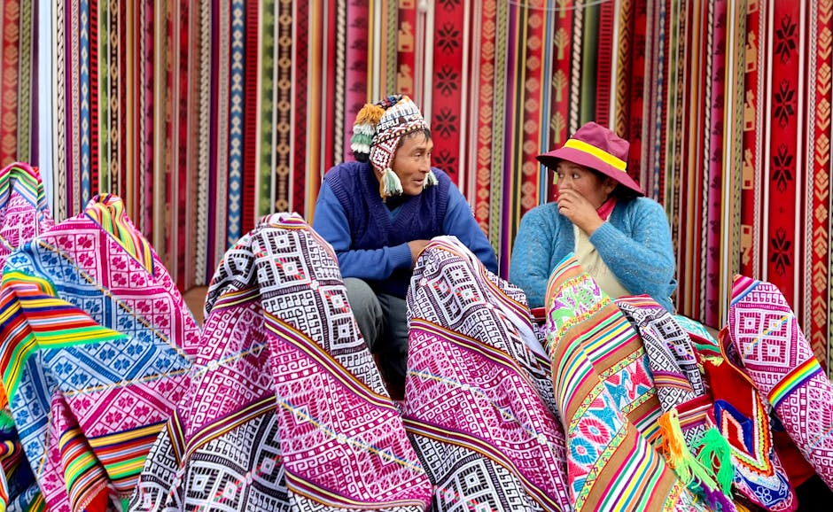 Two vendors surrounded by brightly patterned Andean textiles at market