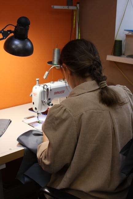 Artisan sewing fabric at a machine under a lamp in workshop
