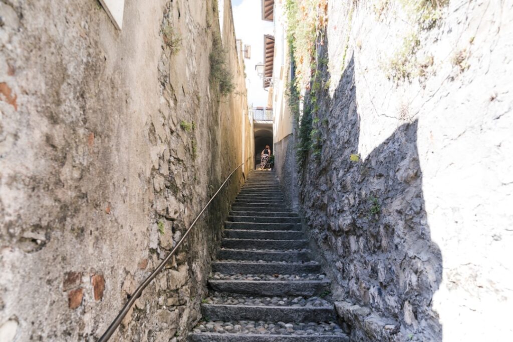 Escalier étroit en pierre bordé de murs anciens, personne poussette en haut à Matera