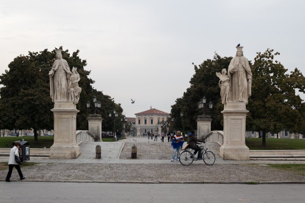 Ingang met twee grote beelden en fietsers bij Prato della Valle, Padua
