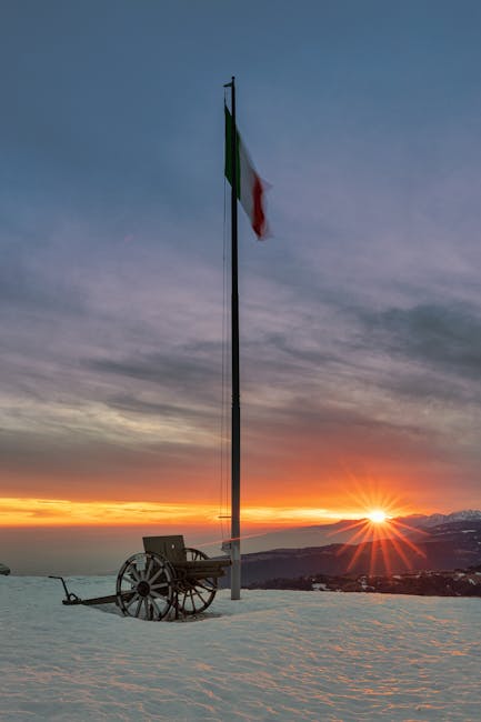 Italian flag and historic cannon on snowy Monte Grappa at sunset