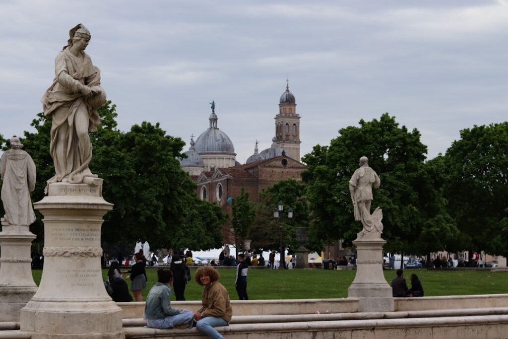 People seated beside statues with Padua basilica domes in background