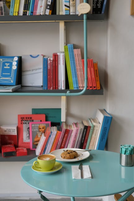 Small round table with latte and chocolate cookie beside stacked books.
