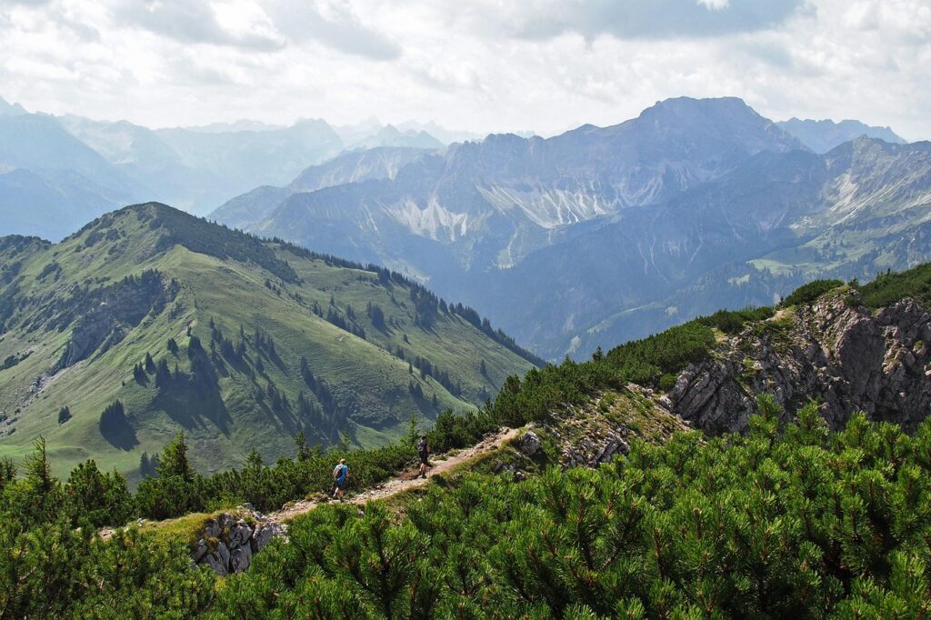 Twee wandelaars op smal bergpad met uitgestrekte groene bergketens