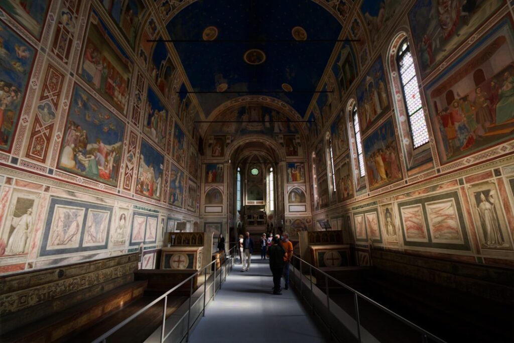 Visitors walking aisle under frescoed walls in Padua chapel