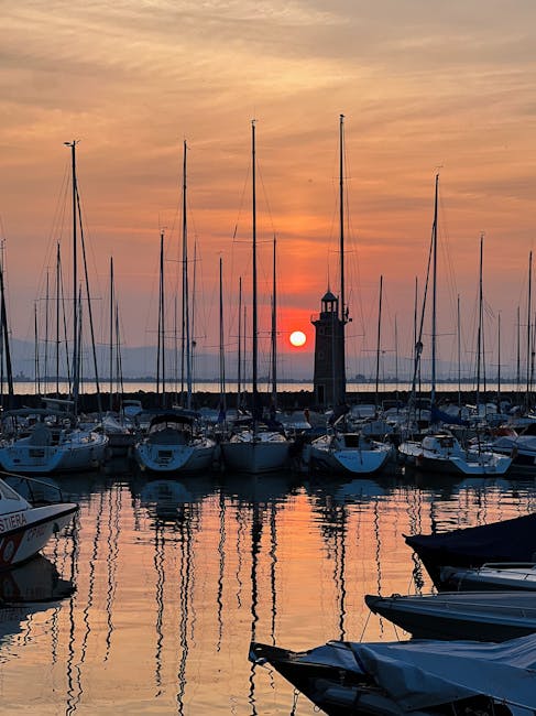 Sunset over Lake Garda marina with sailboats and lighthouse silhouette