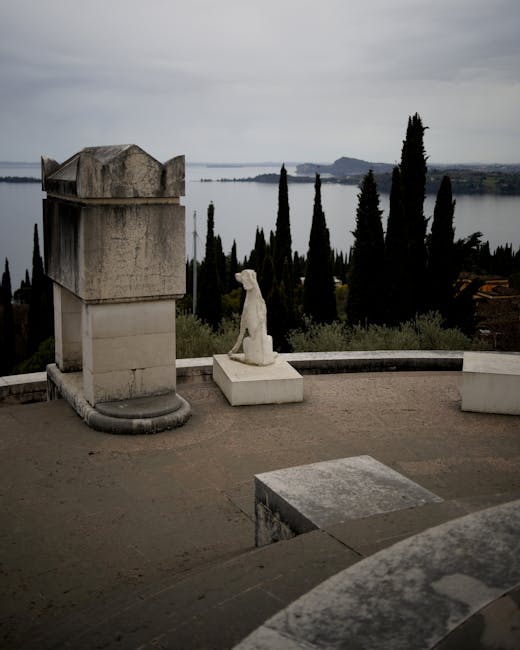 Stone terrace with white dog statue overlooking Lake Garda and cypress trees