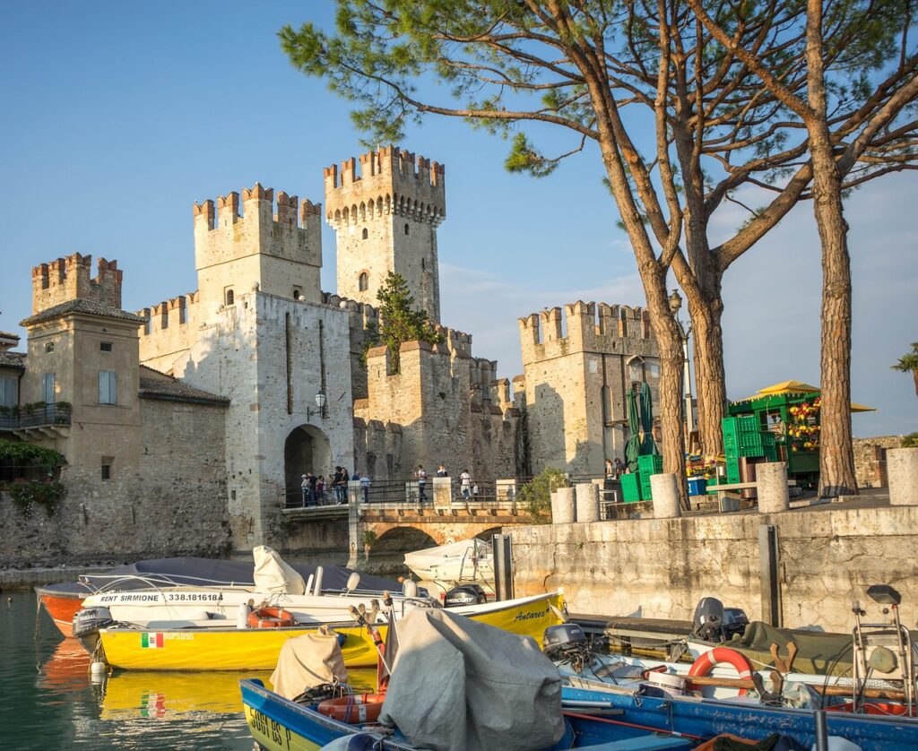 Zamek w Sirmione nad Jeziorem Garda i zacumowane łodzie w porcie.