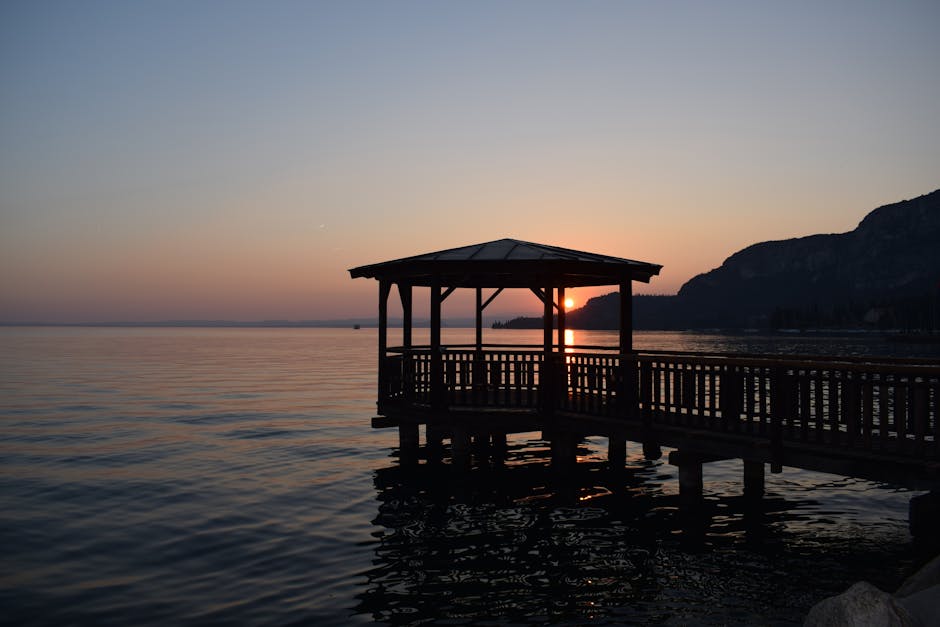 Wooden lakeside gazebo silhouetted against Lake Garda sunset and distant mountains
