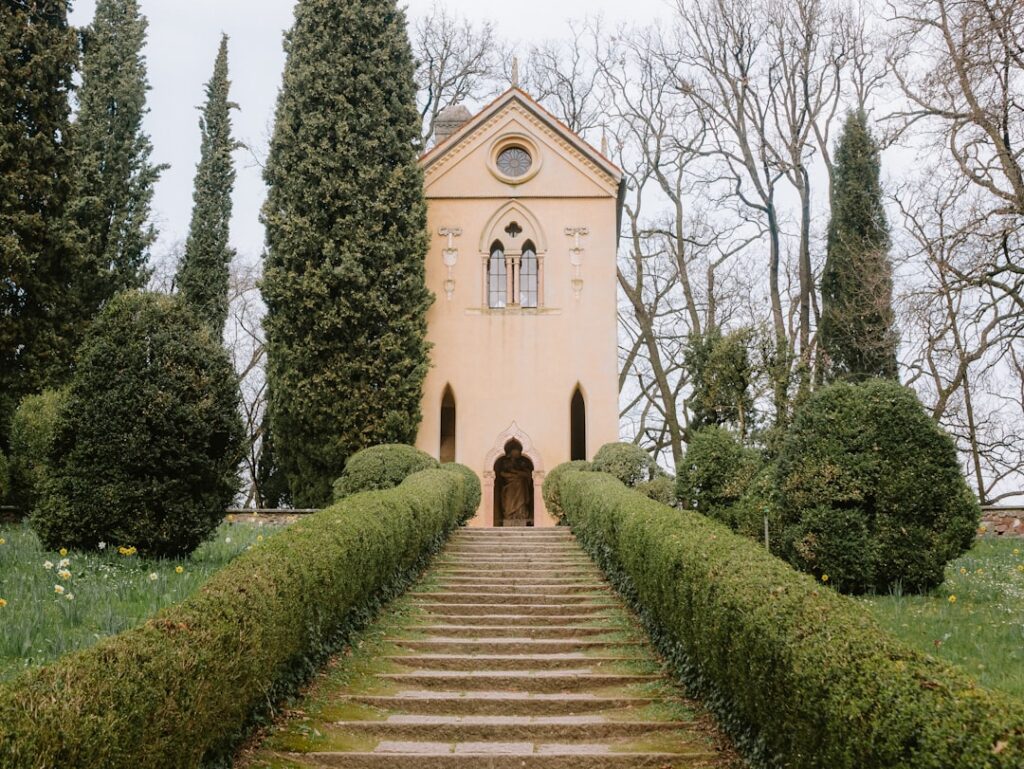 Stone steps framed by trimmed hedges leading to lakeside chapel at Lake Garda