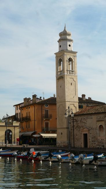 Tall bell tower beside Lac de Garde waterfront with moored fishing boats