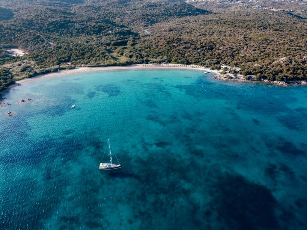 Baia turchese vista dall'alto con una barca a vela al largo in Sardegna