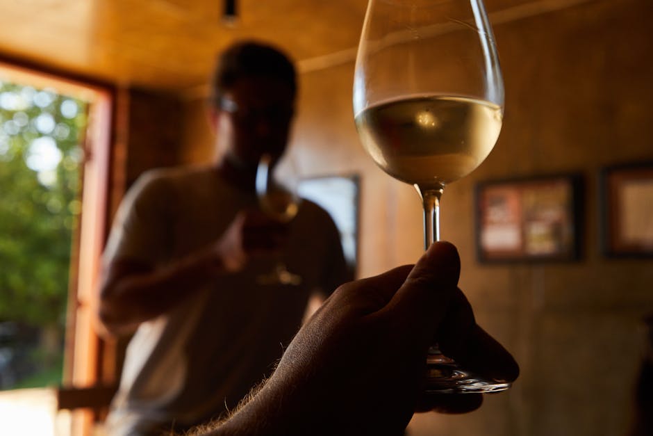 Verre de vin blanc tenu en dégustation en Sardaigne, vigneron flou