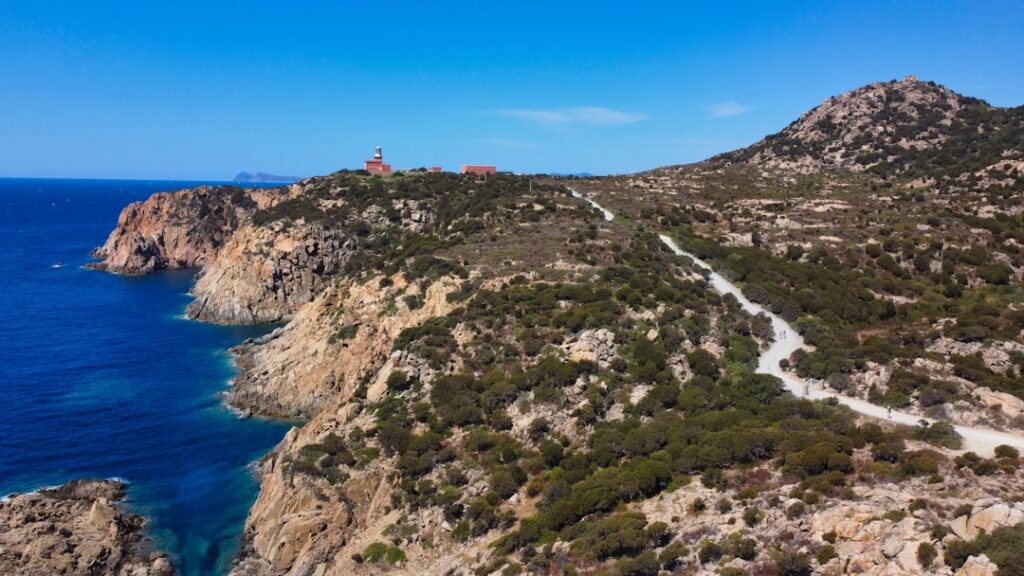 Küstenklippen mit Schotterstraße und entferntem Leuchtturm in Sardinien