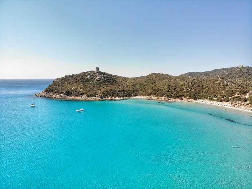 Bucht mit türkisblauem Wasser, Booten und Turm auf Hügeln in Sardinien