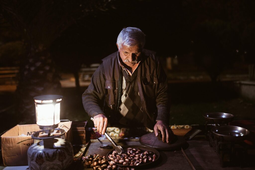 Vieil homme grillant des châtaignes à la poêle, éclairé par une lampe en Sardaigne