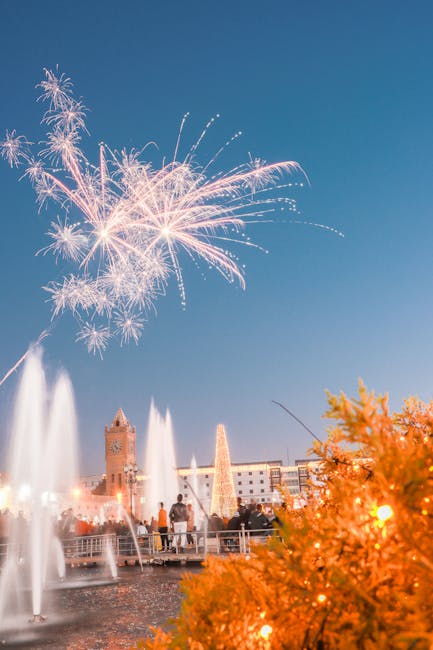 Fireworks burst above fountains and crowds at evening waterfront