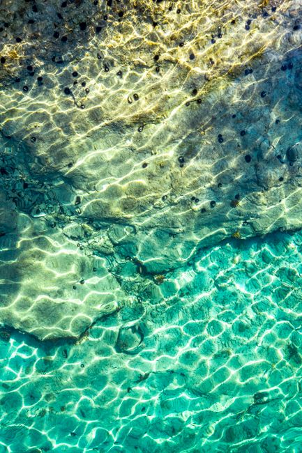 Sunlit shallow Sardinian seabed showing rippling water and dark stones