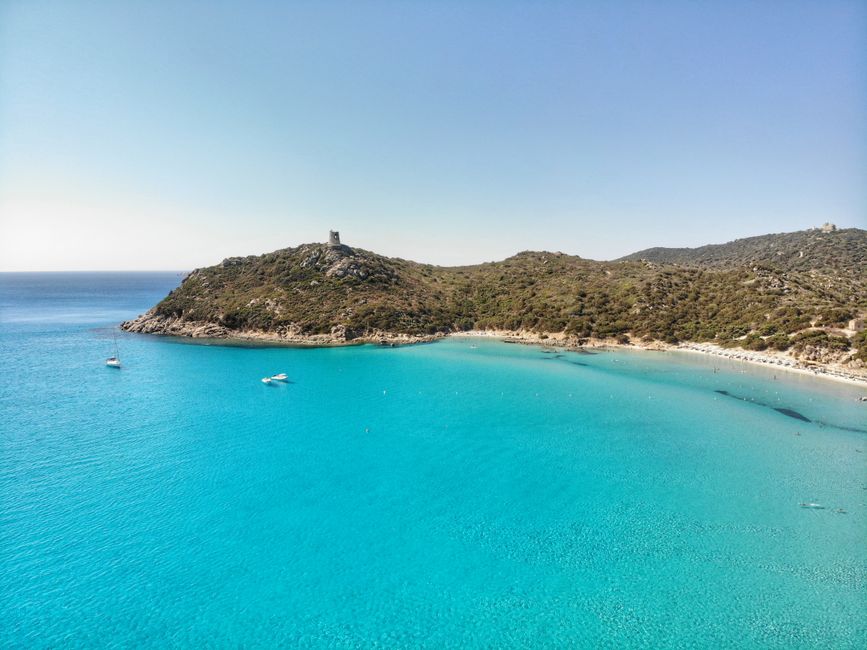 Turquoise bay with hilltop stone tower and boats off Sardinia