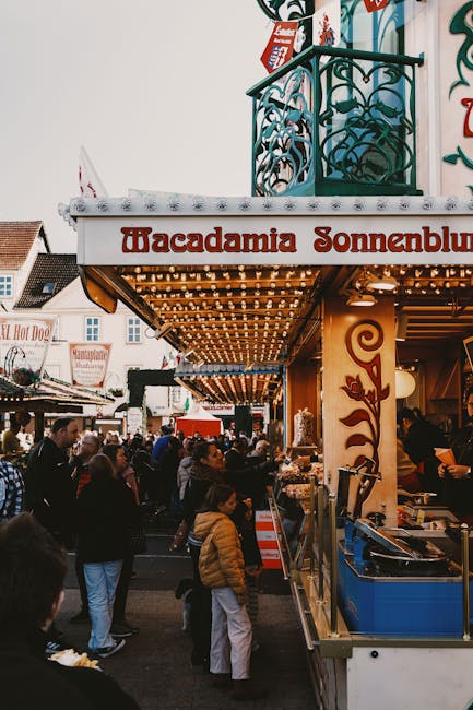 Belebter Jahrmarktstand mit Lichtergirlanden und wartender Menschenmenge.