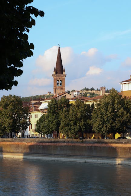 Parma riverside view with tall bell tower and tree-lined embankment